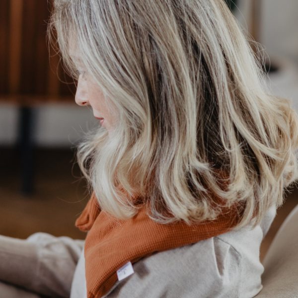 Vrouw op de bank met cognac kleurige warmtesjaal over haar schouders voor ontspanning en warmte tijdens koude dagen.