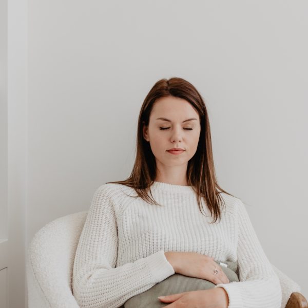 Vrouw zit op een stoel met een warmtesjaal over haar buik voor warmte en verlichting.