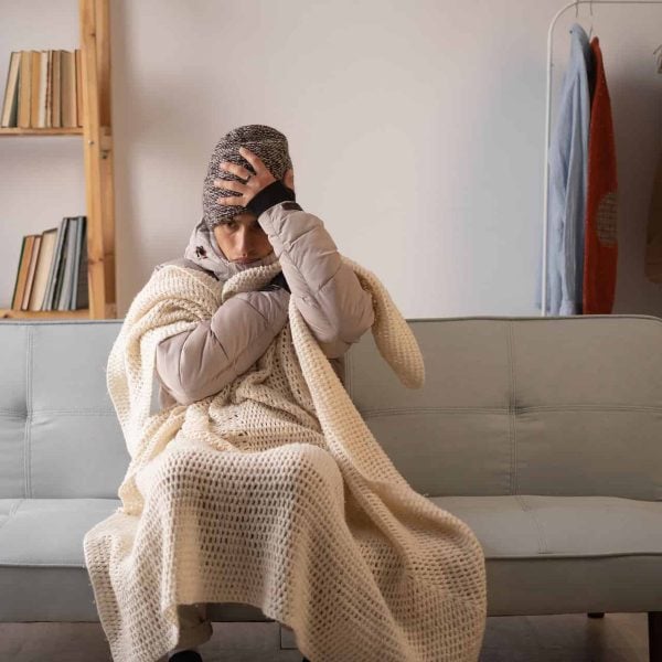 unhappy man feeling cold wearing warm winter clothes indoors. sad broke poor person no to pay electric bill suffering from cold in own unheated home during winter. no heating
