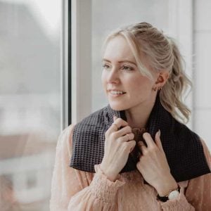 warmtesjaal antraciet wafelstof 70 cm Een jonge vrouw warmt zich om door een warmtesjaal over haar schouders te leggen en kijkt dromerig uit het raam.